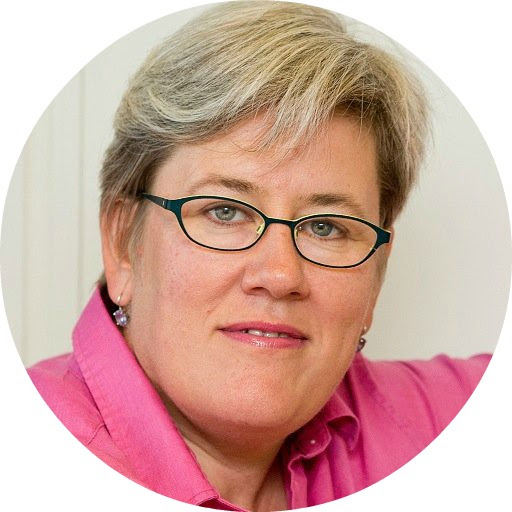 Headshot of a smiling woman with short gray hair, glasses, and a pink shirt