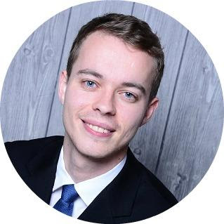 Headshot of a smiling young man in a dark suit and blue tie