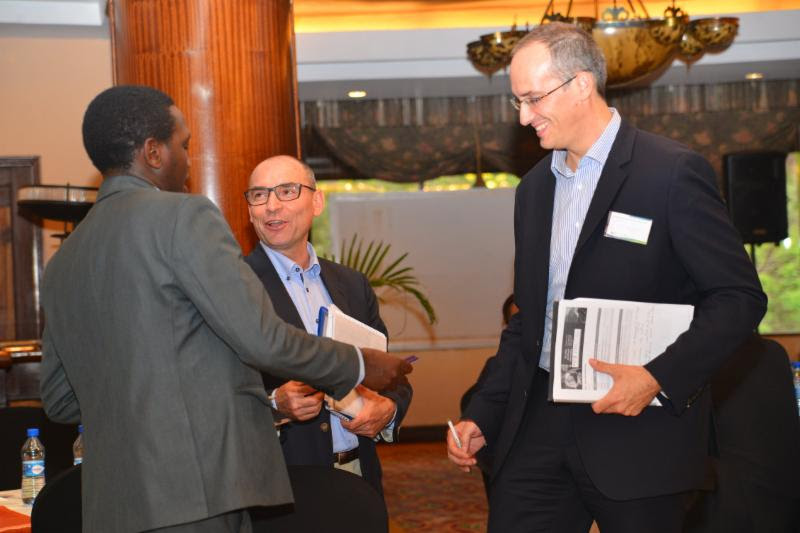 Three attendees in suits talking and exchanging notes at an energy access networking event